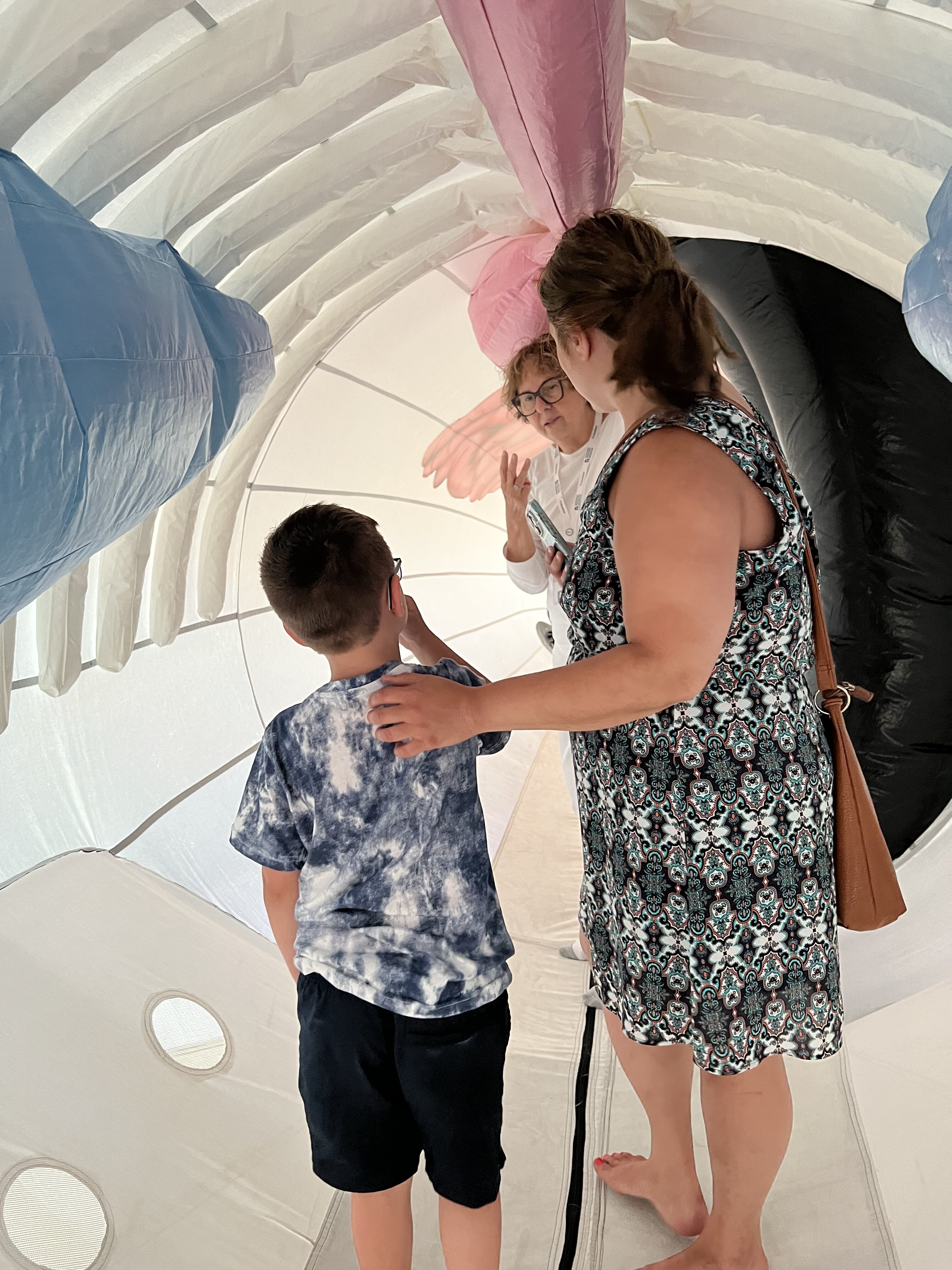 Three people, including a child and two adults, stand inside a large inflatable whale. The interior of the whale is designed with colorful representations of organs and tissues.