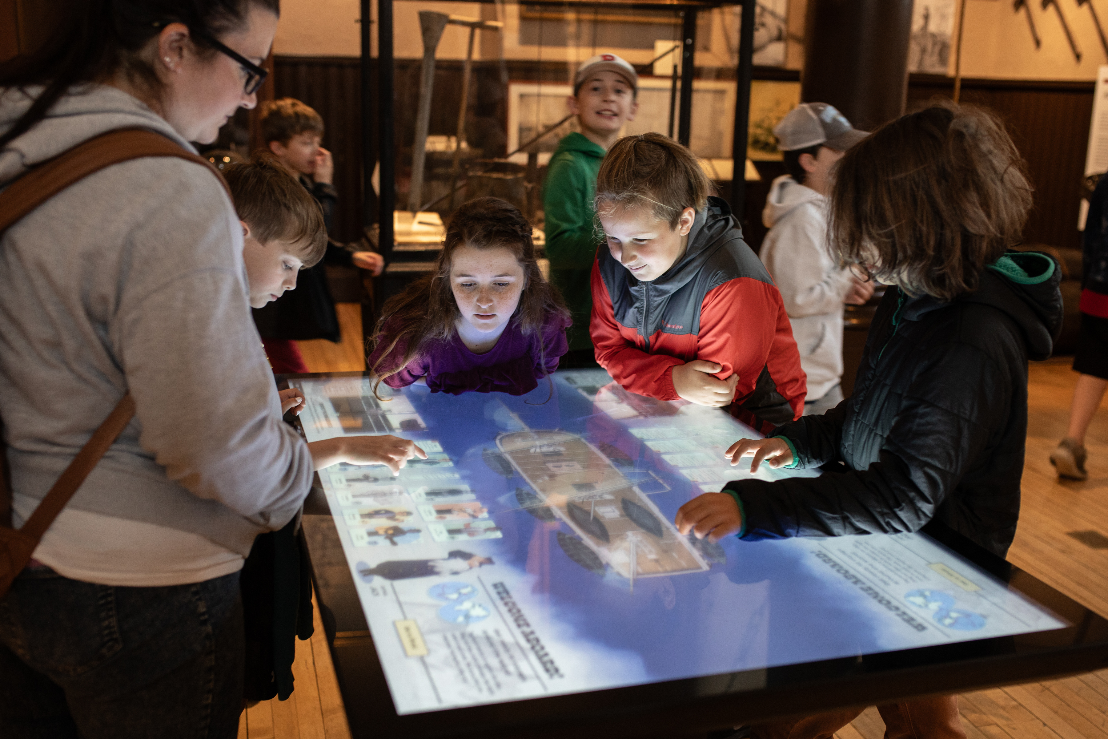 Children gathered around an interactive digital table, engrossed in an educational game about whaling voyages around the world.