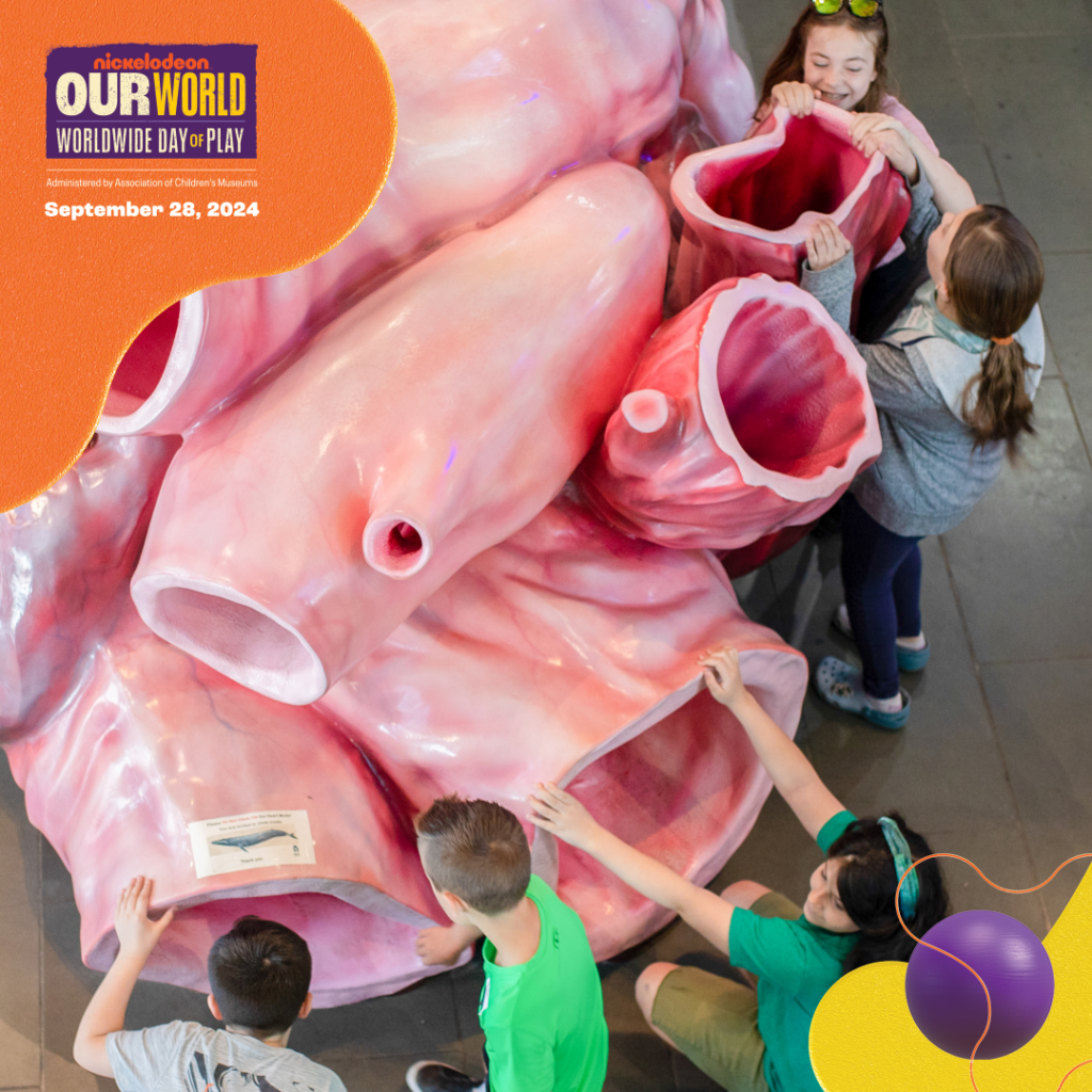 Children interacting with a large sculpture of a whale heart during Nickelodeon’s 'Worldwide Day of Play' event. The realistic sculpture showcases the intricate anatomy of a whale's heart. A sign in the top left corner announces the event date: September 28, 2024.