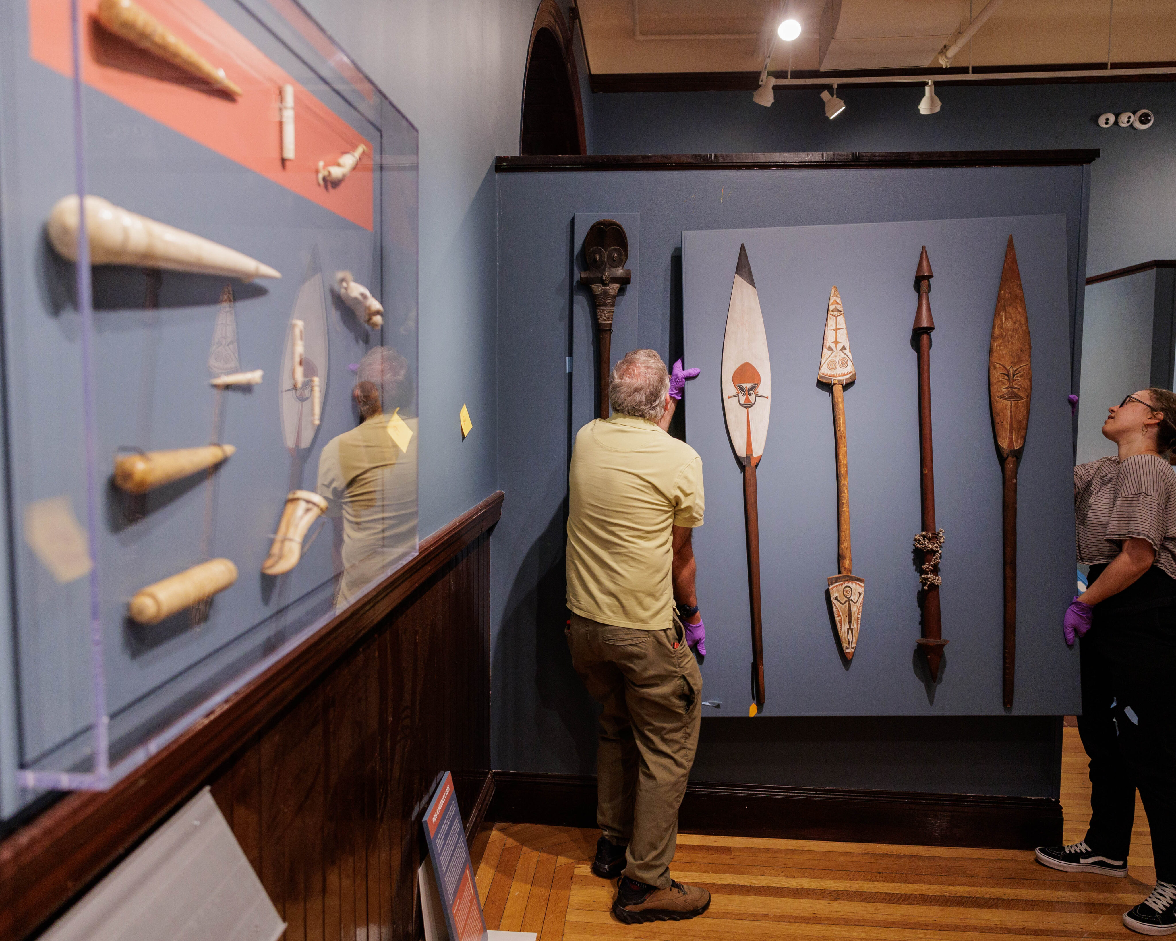 NBWM Curator Melanie Correia and installer Scott Benson hang a case with Pacific paddles and dance wands during installation for The Wider World & Scrimshaw. 