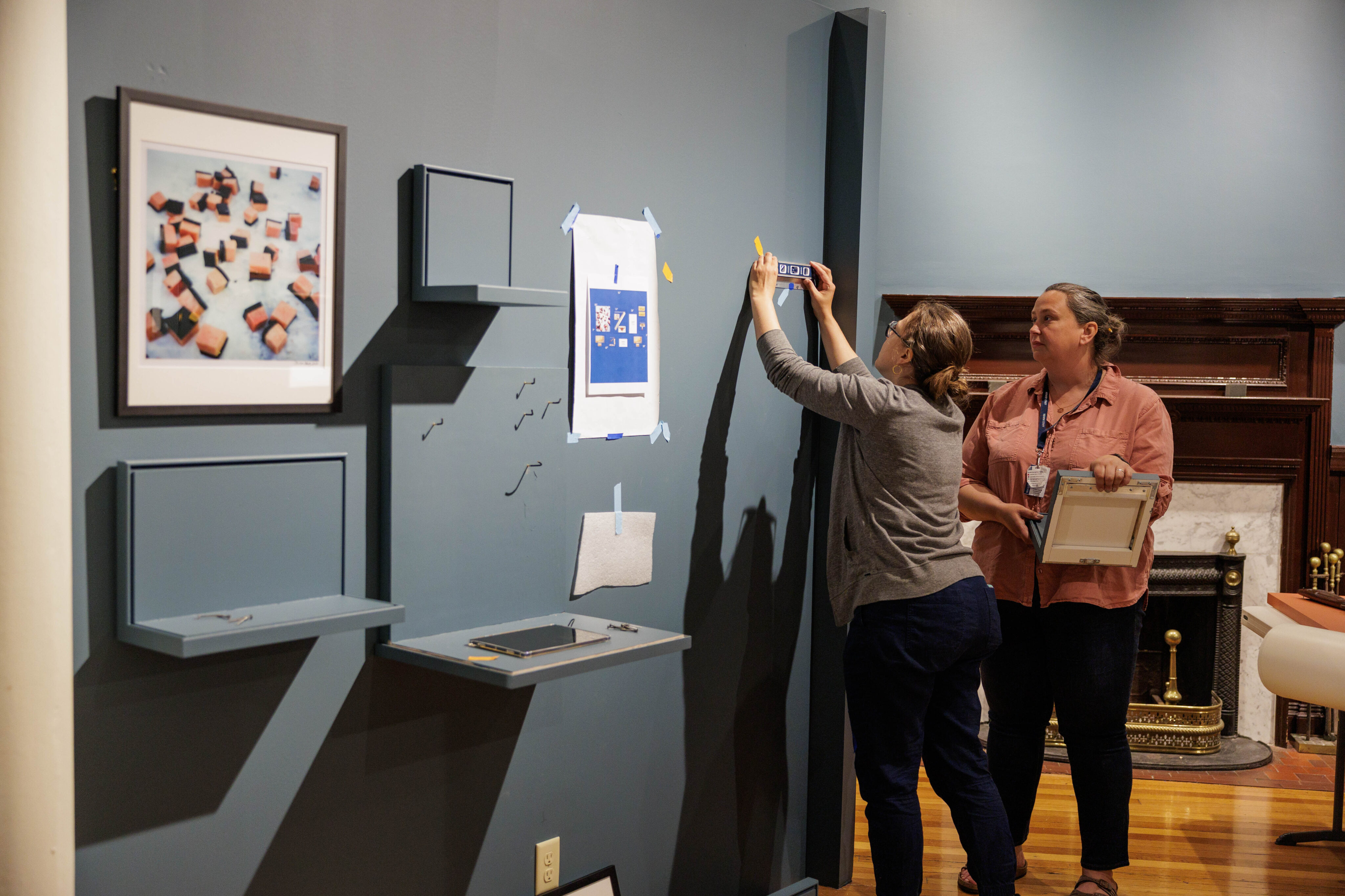 NBWM Curator Melanie Correia and Chief Curator Naomi Slipp hang a case for the Whale Cosmologies section during installation for The Wider World & Scrimshaw. An image of Muktuk by photographer Brian Adams is visible in the foreground. 